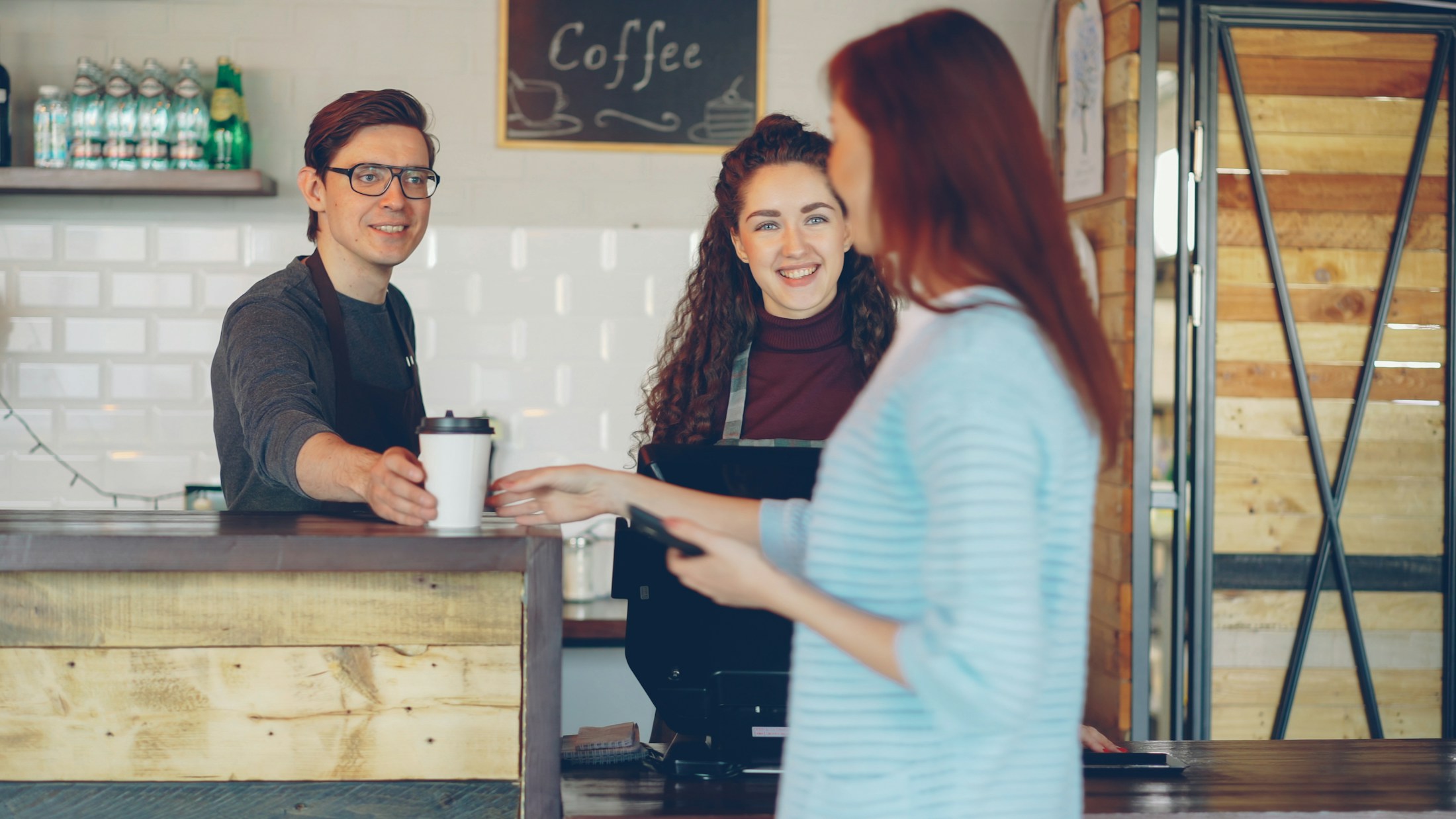 A barista hands a coffee to a customer.